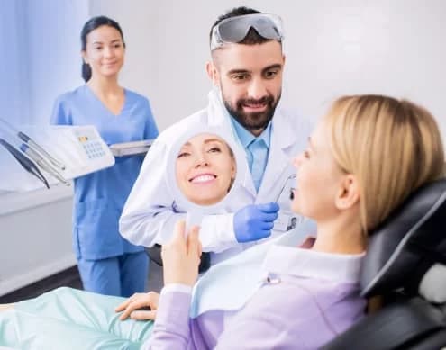 A Kayan dentist showing a patient her smile in a mirror, with a dental assistant beside them